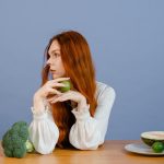 Thoughtful woman with broccoli, melon, and lime on a table.