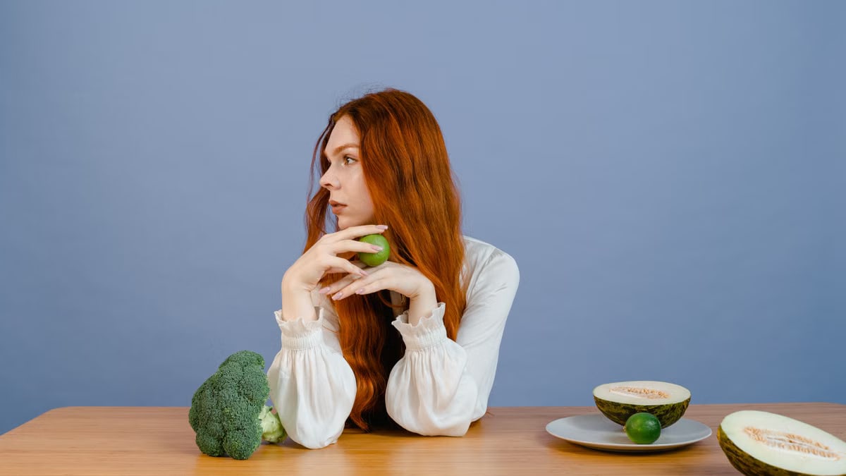 Thoughtful woman with broccoli, melon, and lime on a table.